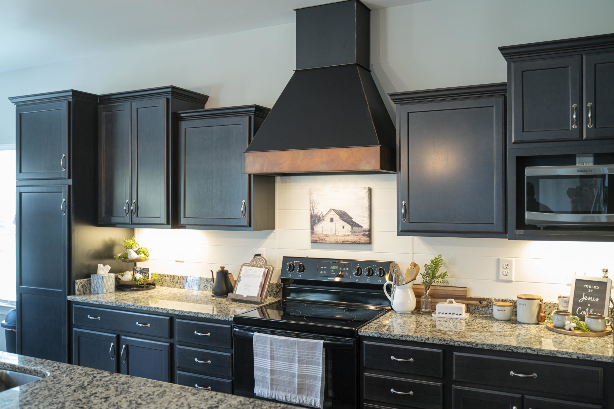 A Brushed Black Range Hood created by Stoll Industries in a dark kitchen remodel.