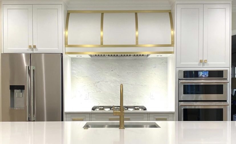 A kitchen remodel features a white range hood with hold accents from Stoll Industries.