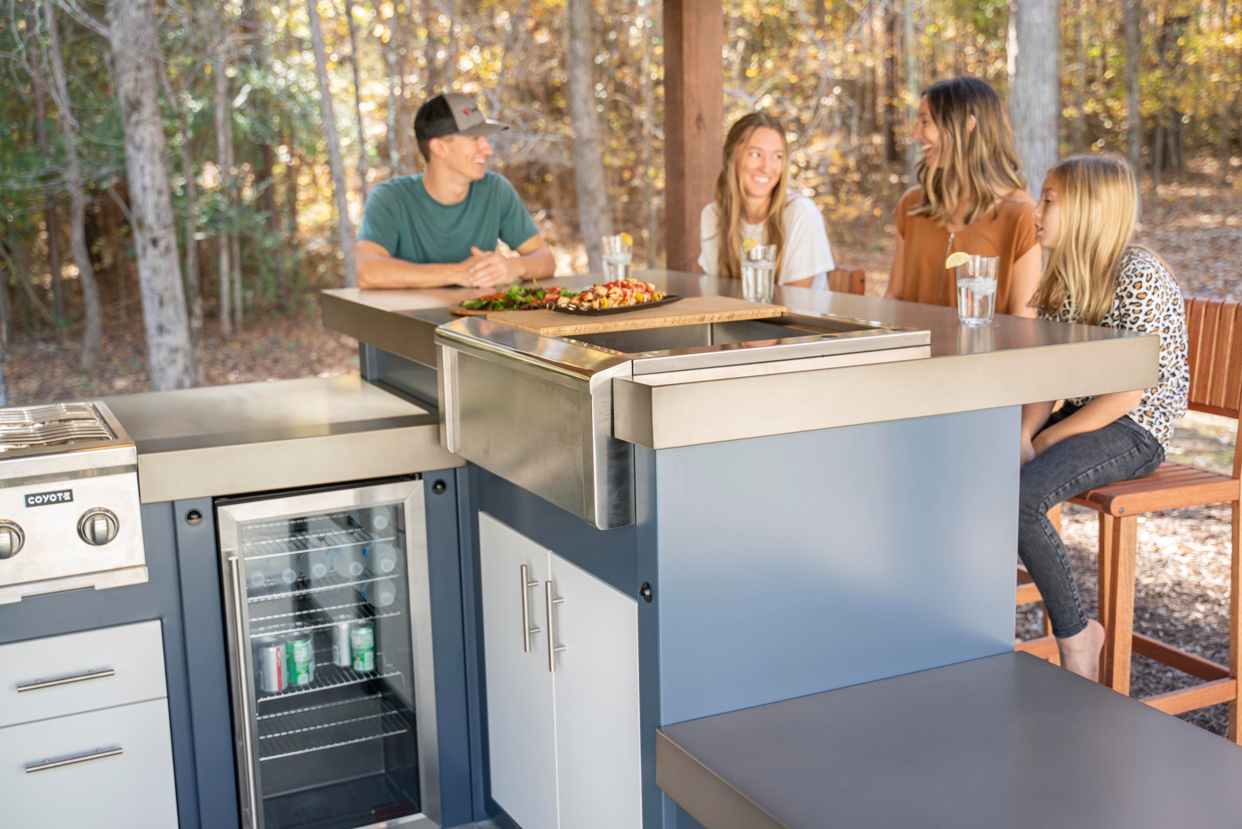 A group of people sit around a Stoll Industries outdoor kitchen enjoying outdoor living.