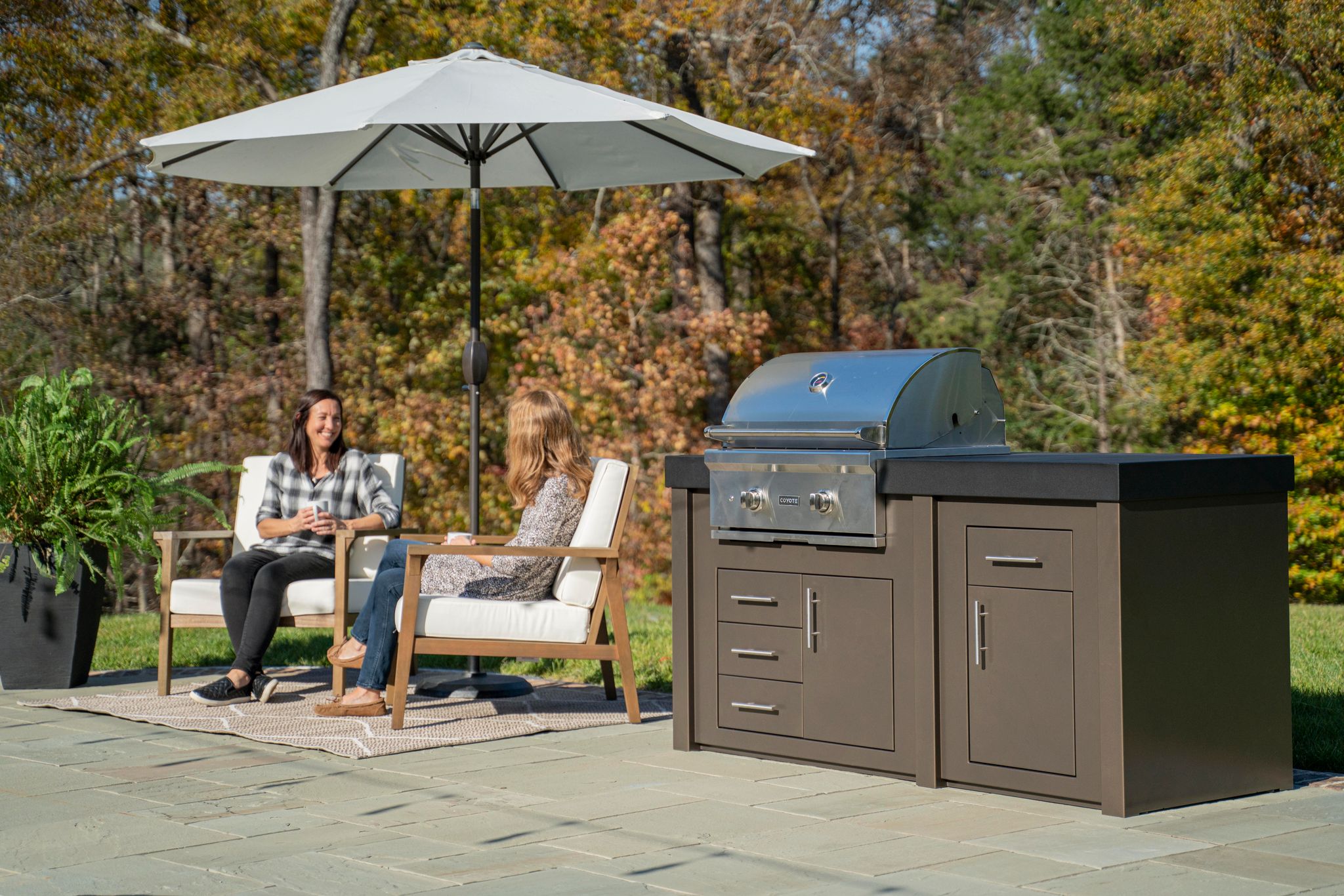 Two women sit by a Stoll Industries outdoor kitchen enjoying outdoor living.
