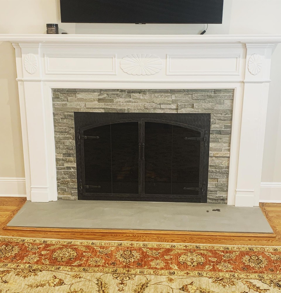 A renovated fireplace in stone, featuring forged iron fireplace doors by Stoll Industries.