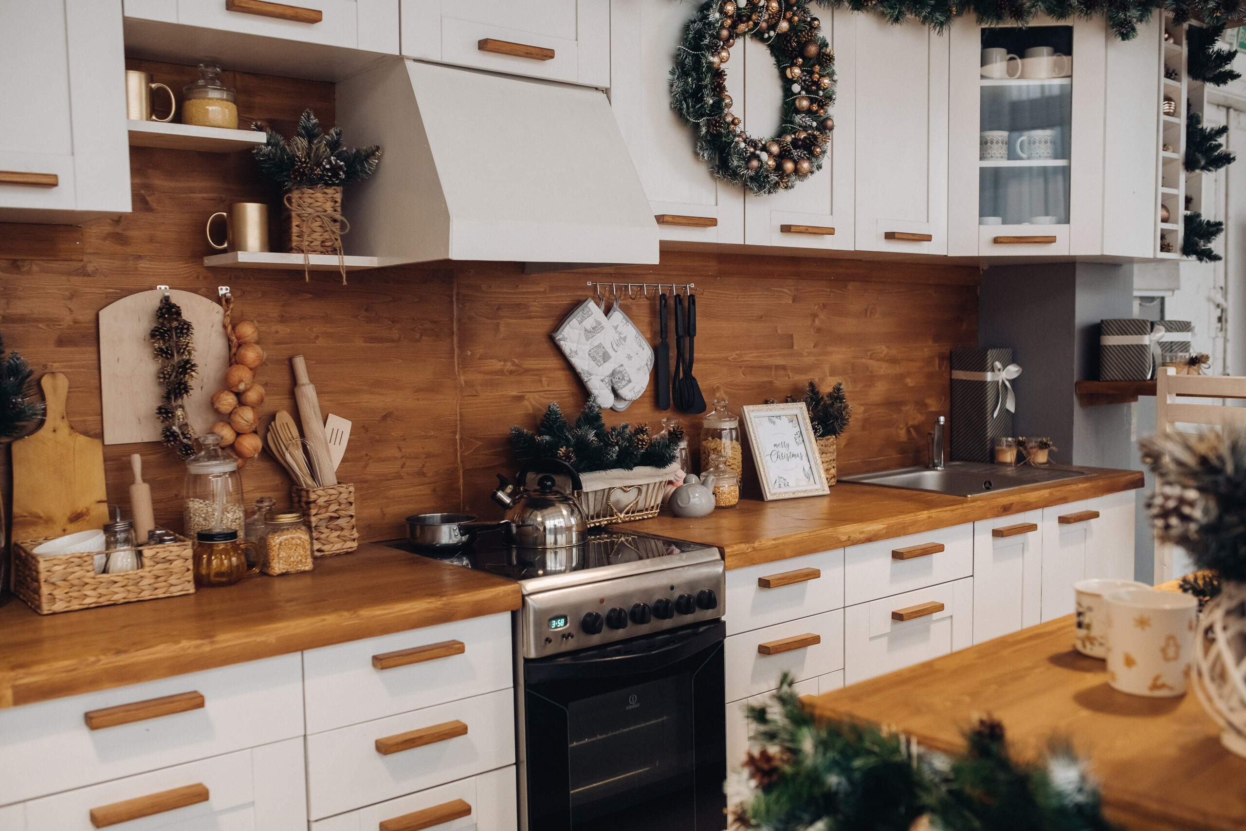 Close-up of modern cozy kitchen in white and brown colors with stuff, cooker and decorative fir tree branches. Christmas decorations.